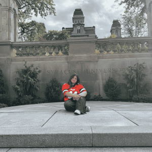 Student sitting into front of Syracuse University sign in front of Hall of Languages.